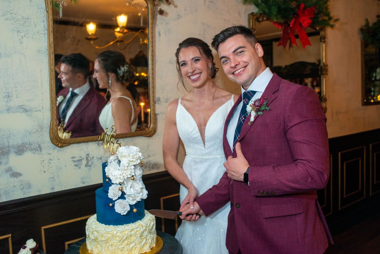 A wedding couple poses next to their elegant blue and gold tiered wedding cake at their reception.