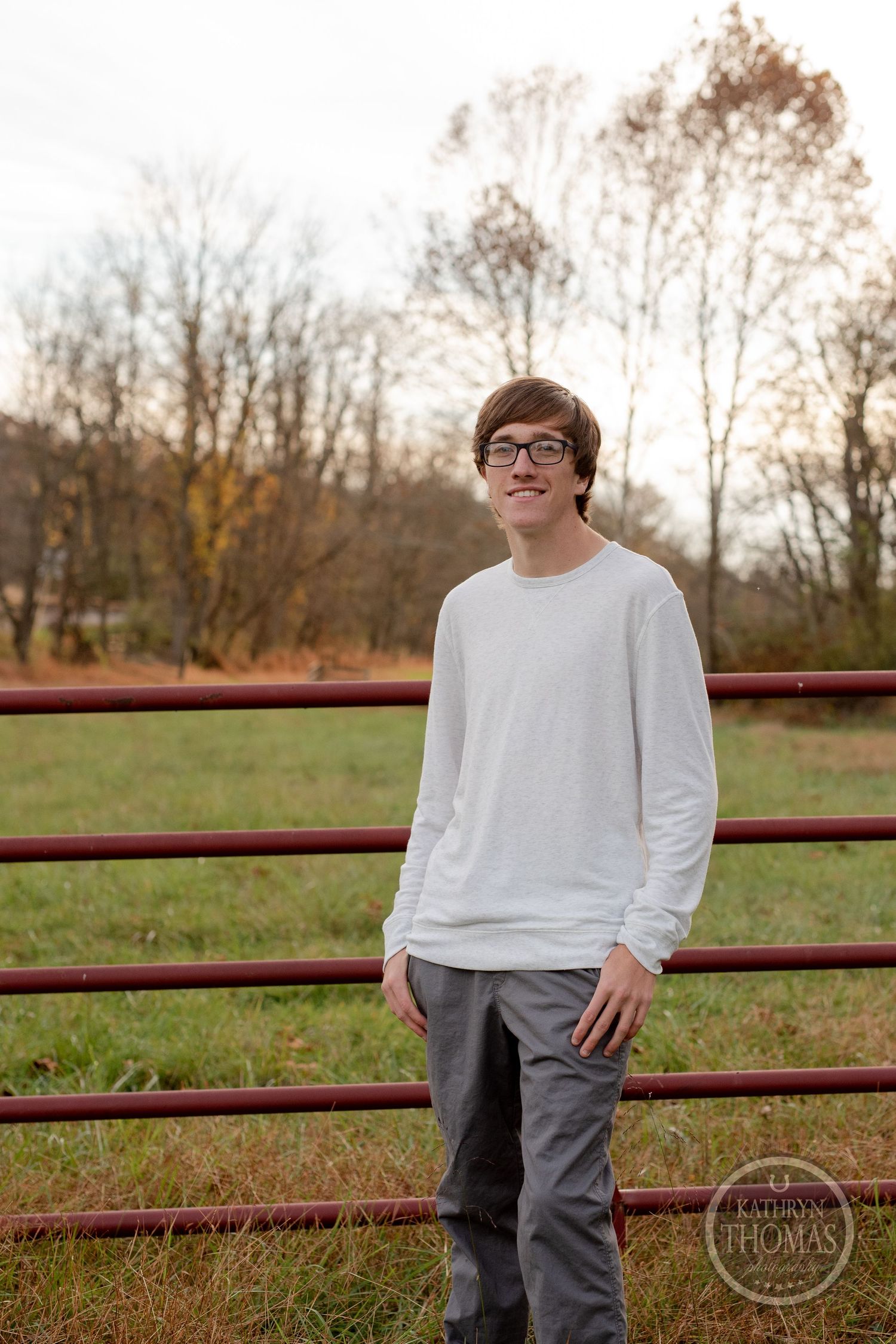Casual outdoor portrait against rustic fence with fall foliage in background.
