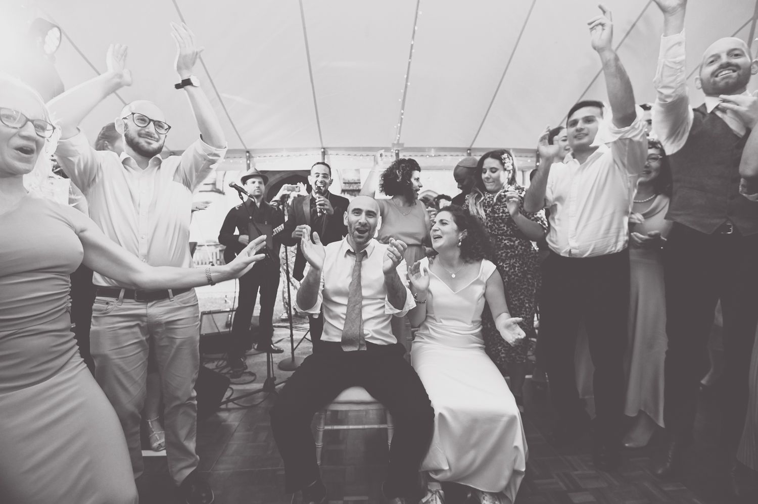 Energetic wedding reception dance party under white tent with guests celebrating.