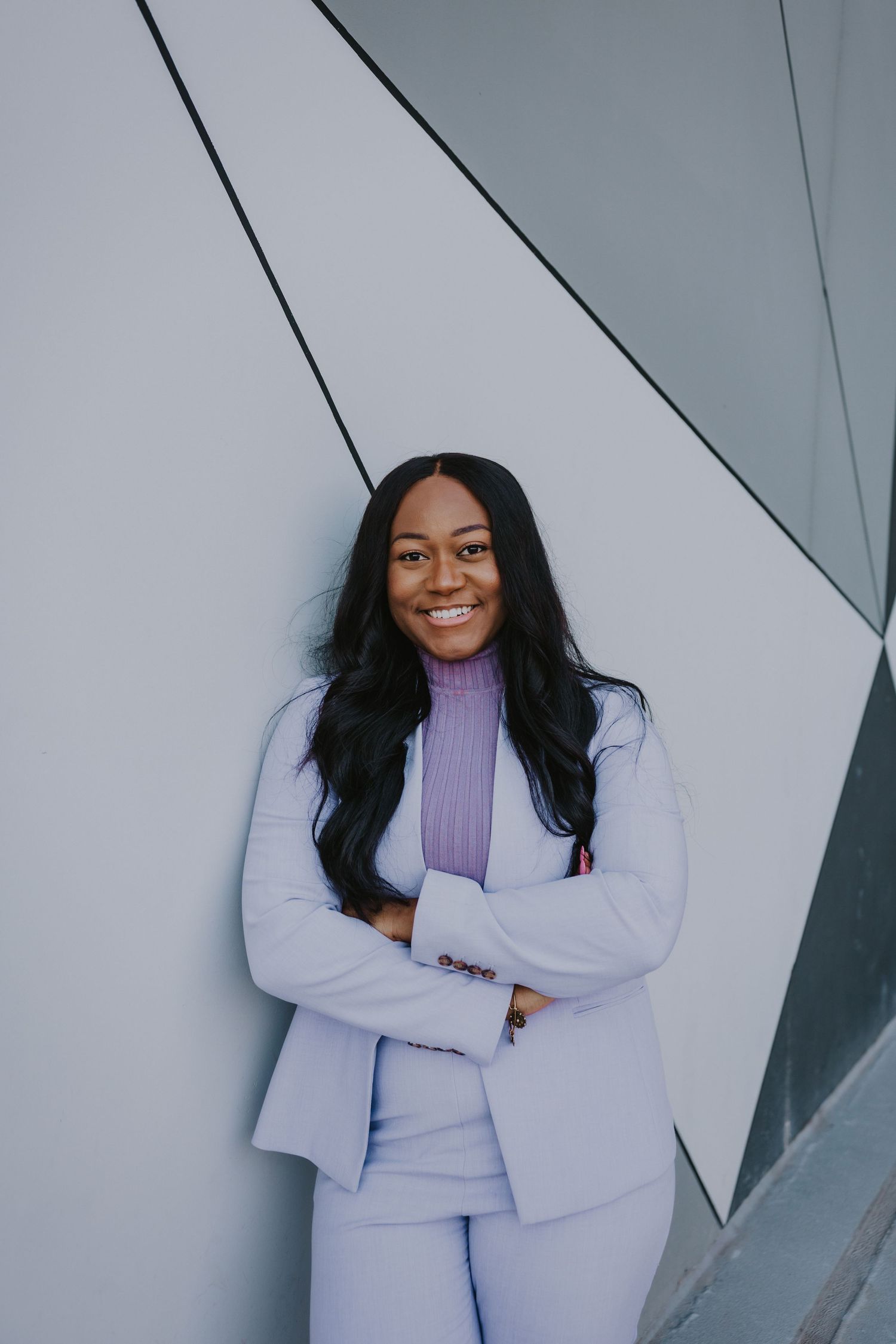 Portrait of someone in lavender suit smiling against modern geometric wall.