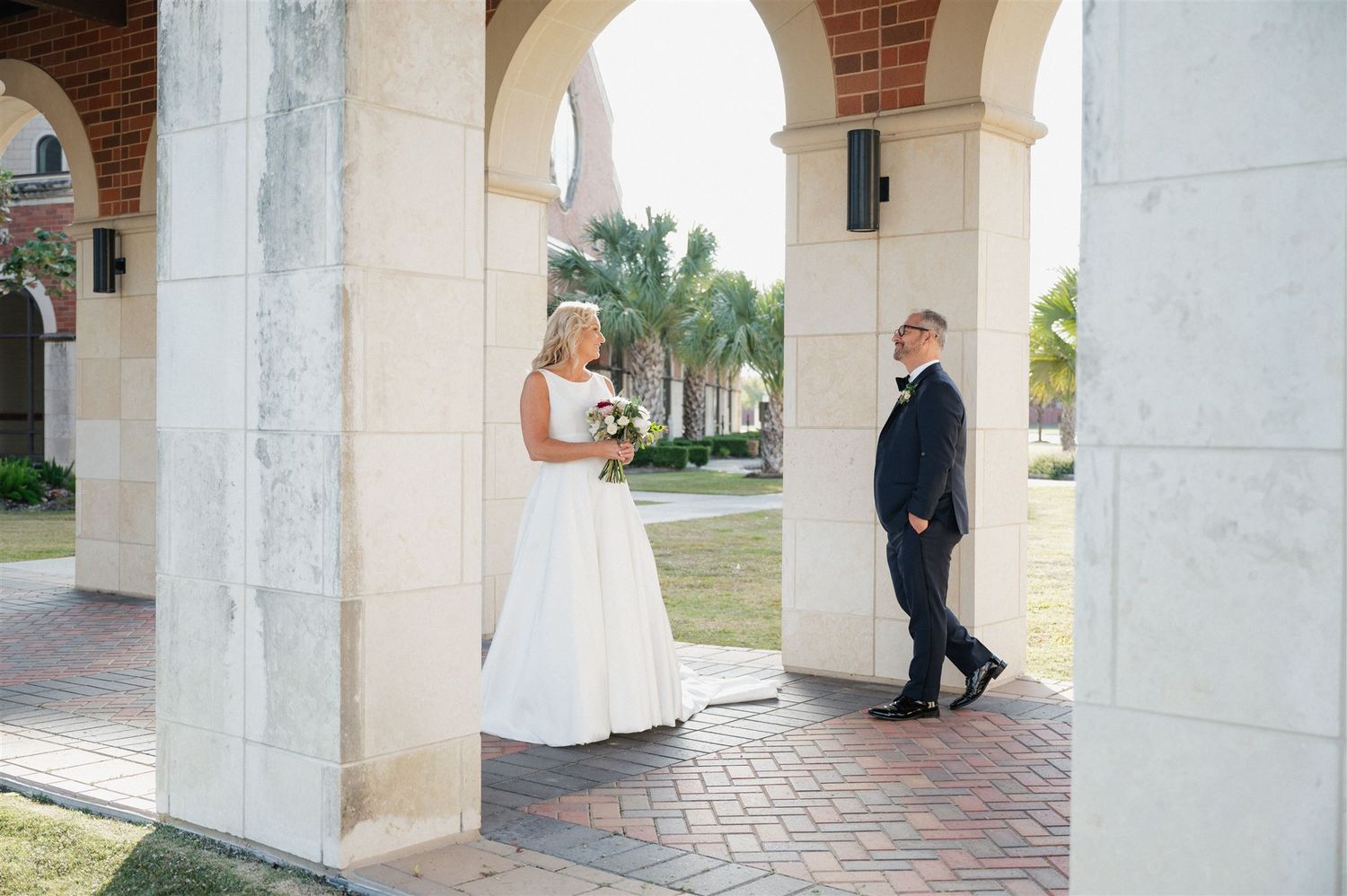 A couple shares a moment under elegant stone arches during their wedding.
