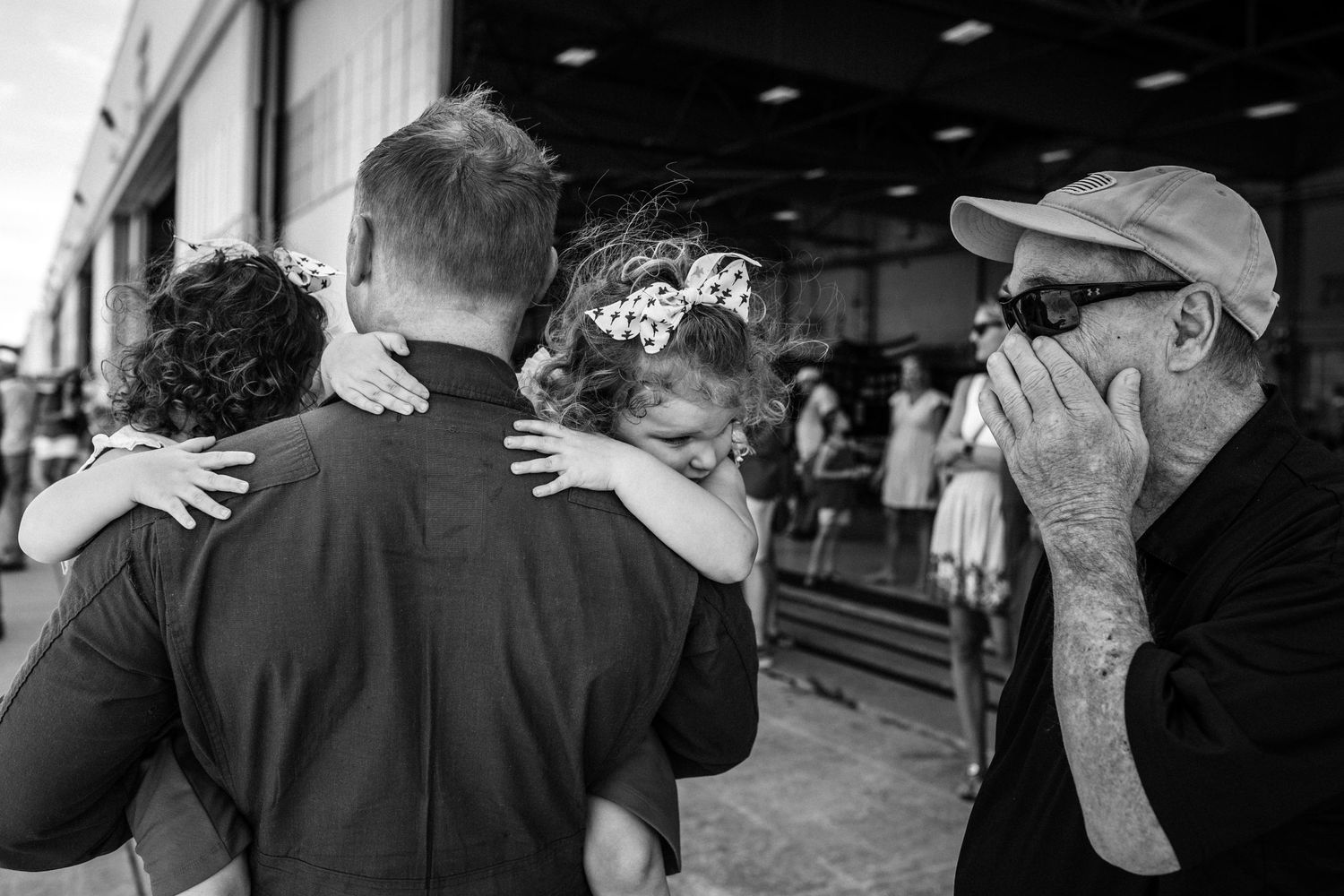 dad carrying daughters at naval military homecoming and grandpa wiping away tears