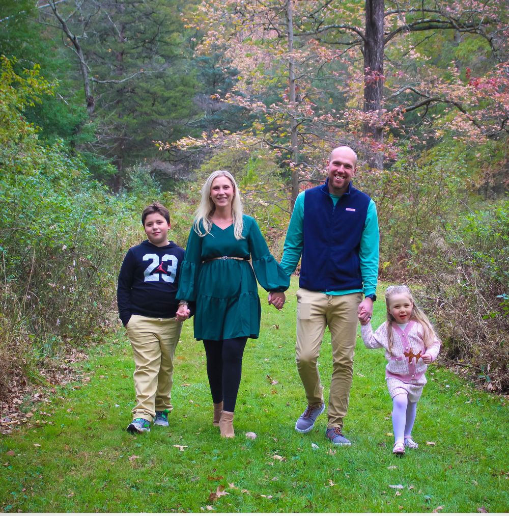 A family of four walking hand in hand on a wooded trail in autumn.