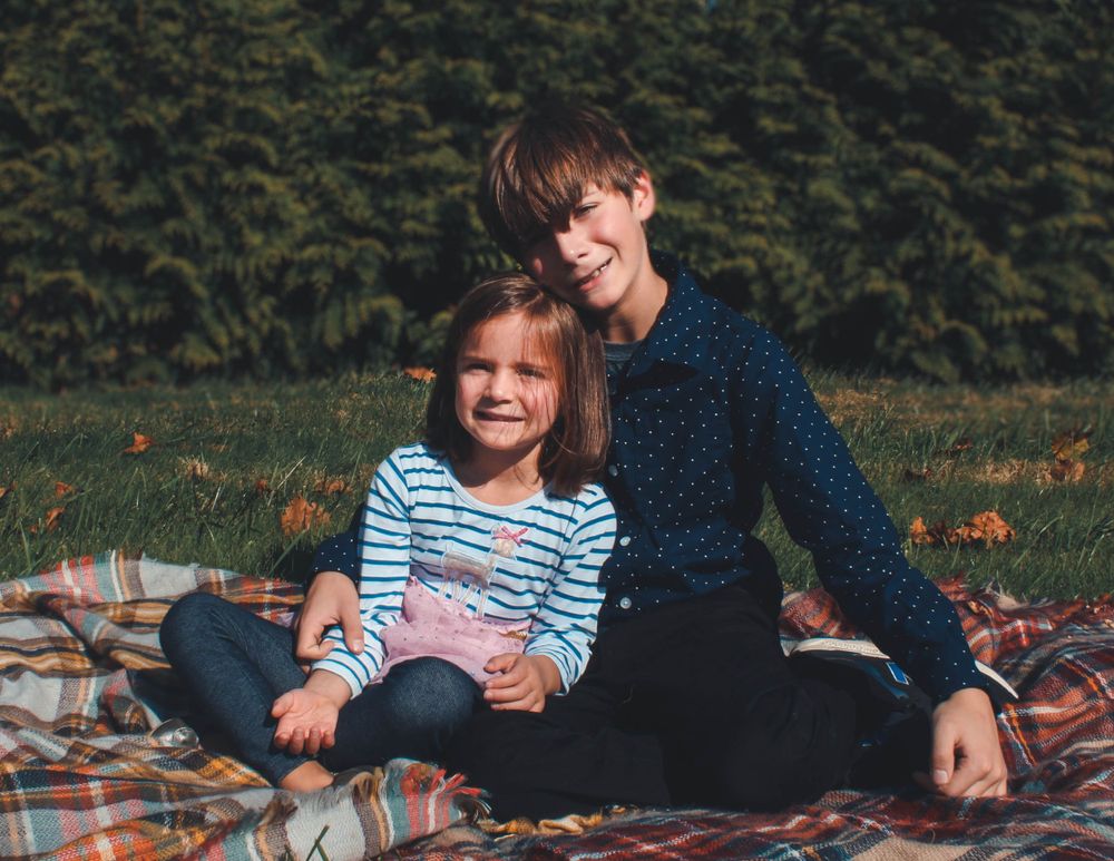 Two children on a blanket having a picnic outdoors.