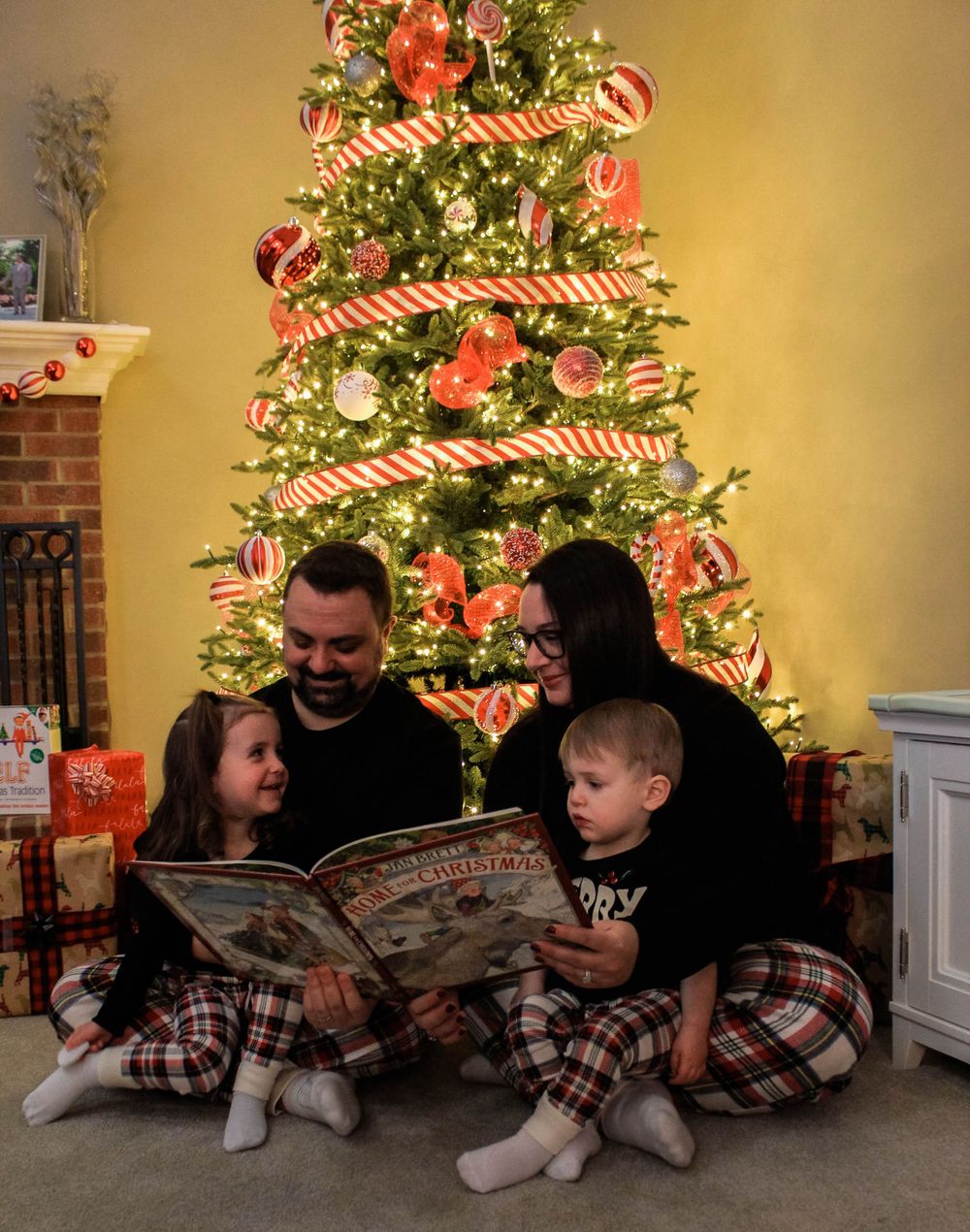 Family reading a book together by a decorated Christmas tree with candy cane ornaments.