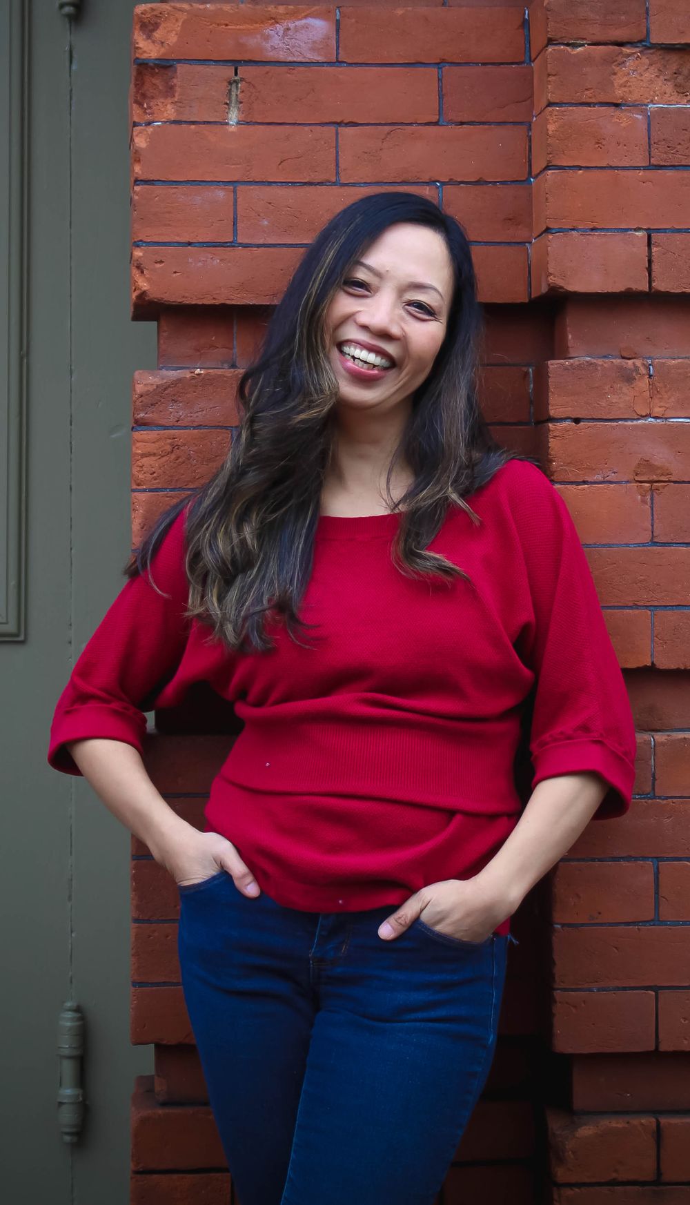 Woman in red sweater smiling against brick wall background.