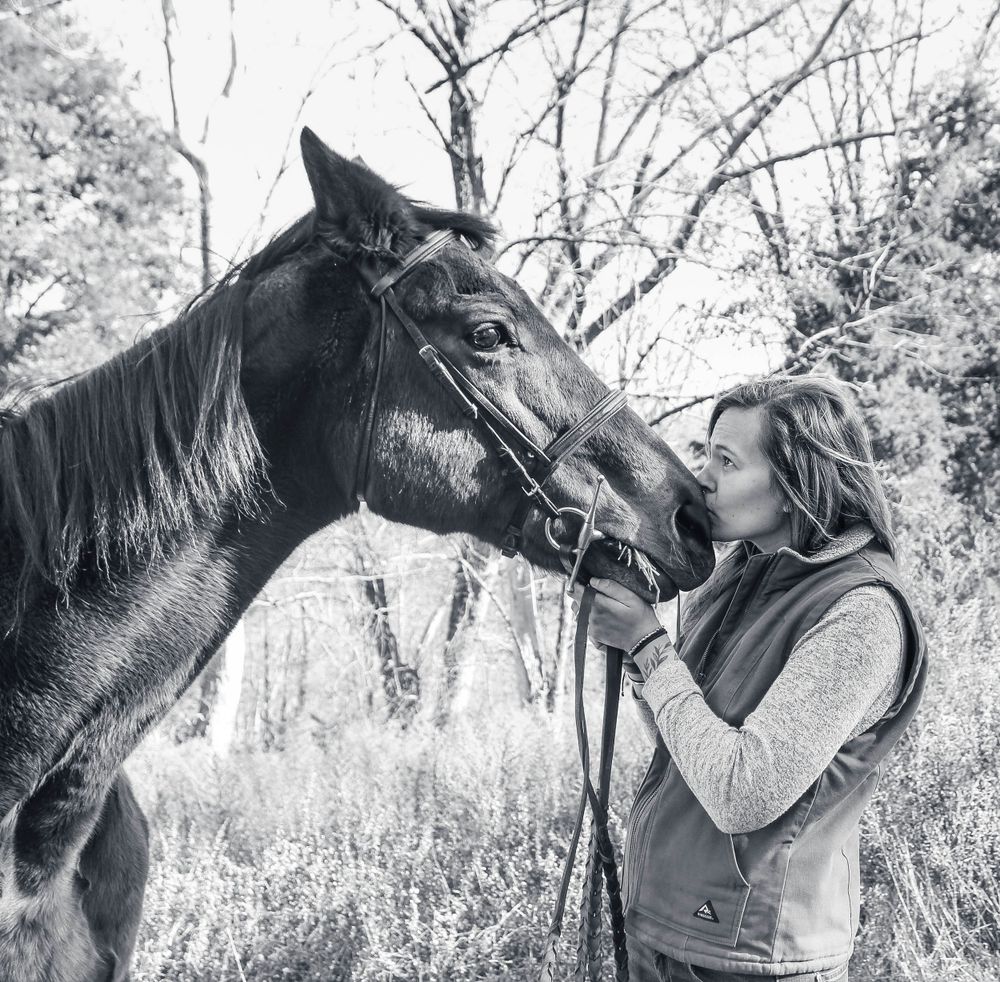 Black and white photo of person with horse in winter woodland setting.