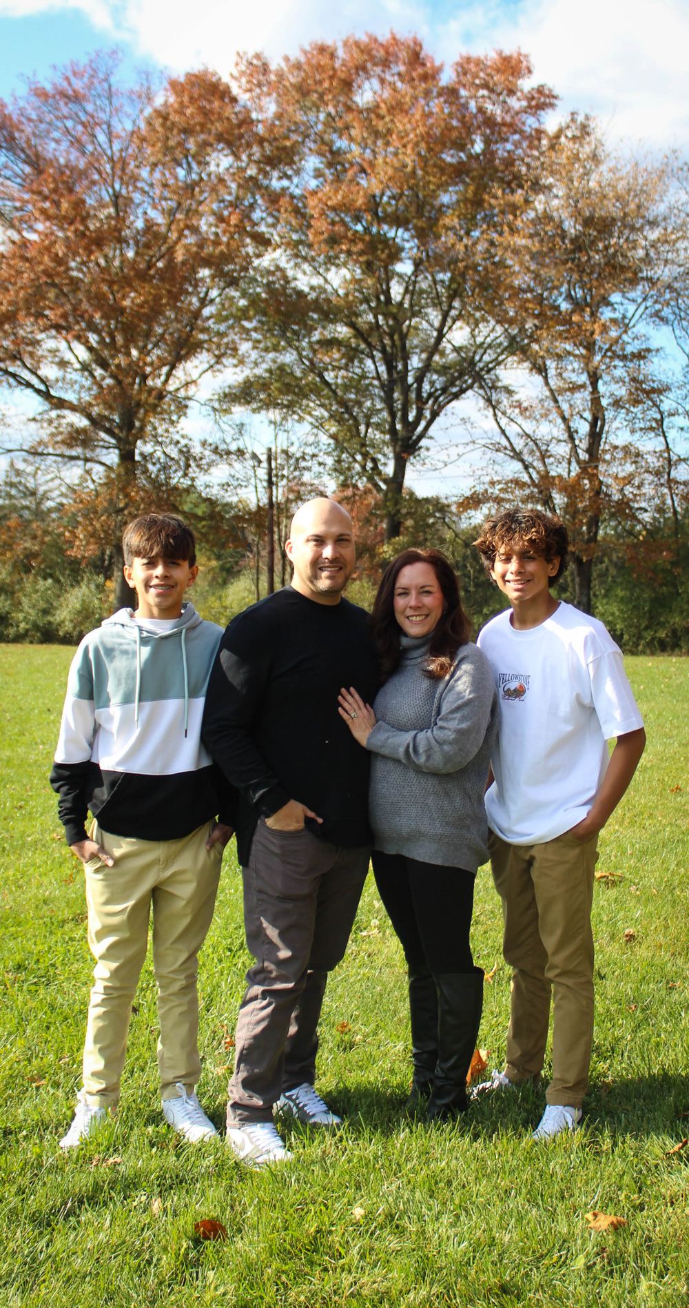 Family of four poses outdoors with fall foliage in the background.