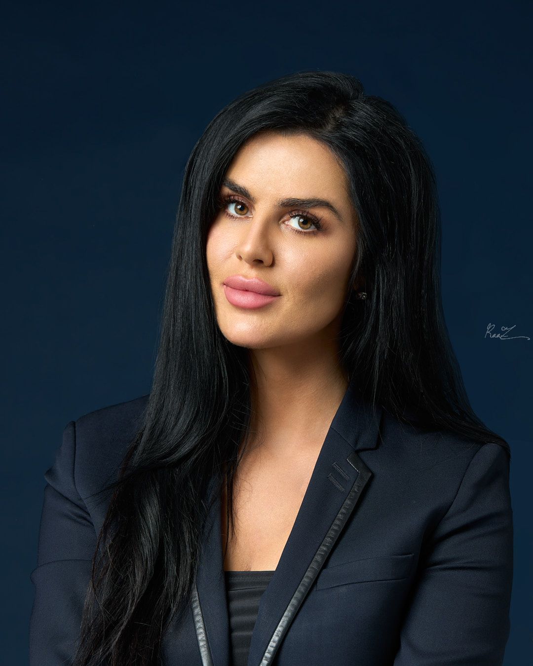 Professional studio portrait against a dark blue background wearing a black blazer.
