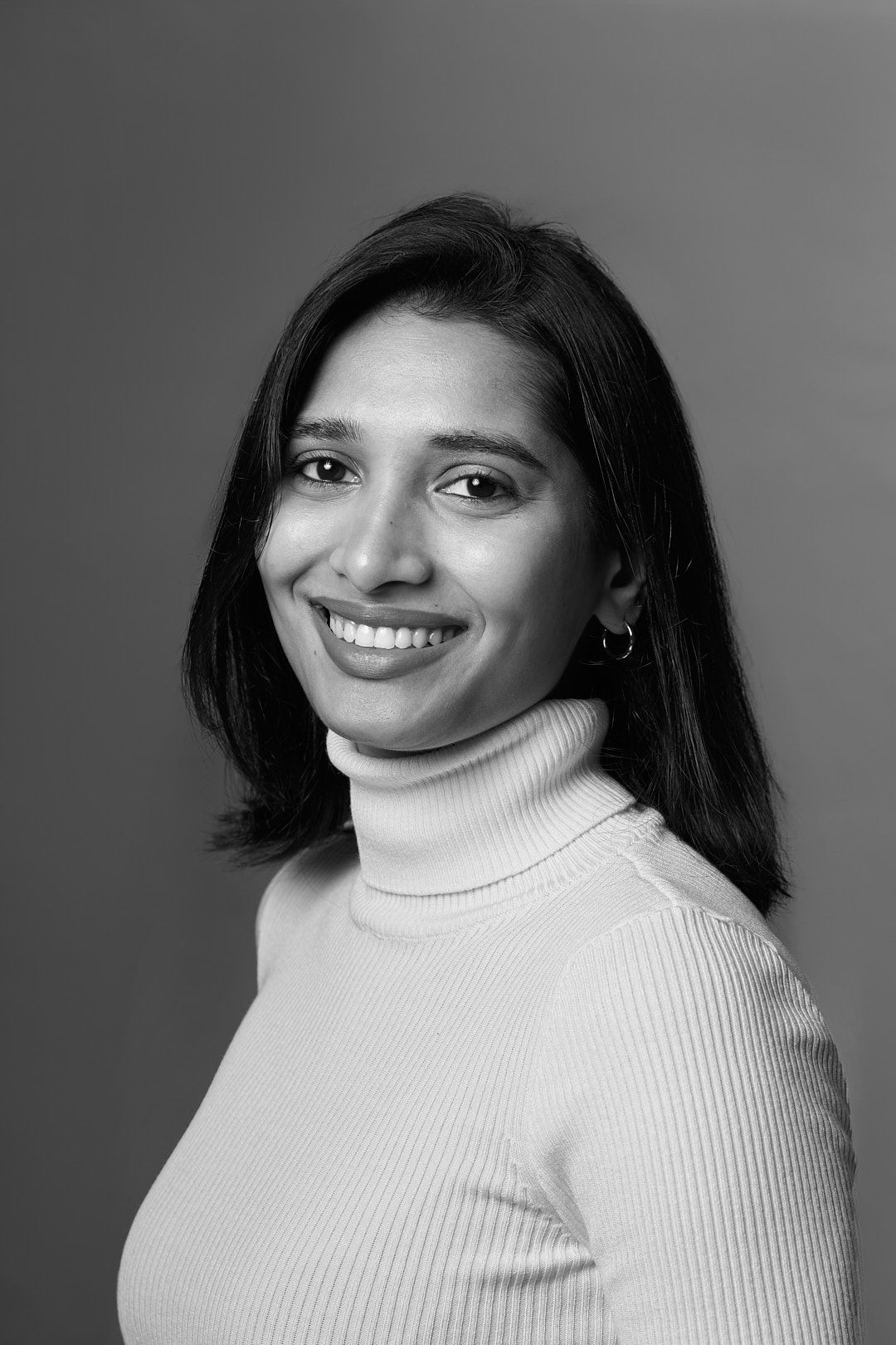 Portrait in black and white featuring a white turtleneck sweater against a grey background.