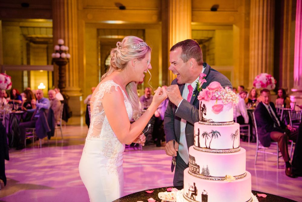 Candid photo of a bride and groom sharing a funny moment while cutting their elegant Wild Flour wedding cake at Cleveland City Hall in Ohio.
