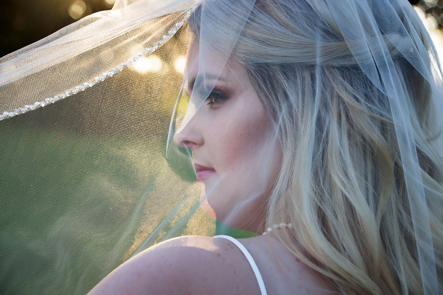 A dreamy profile portrait of a person with blonde hair and a veil in golden sunlight.