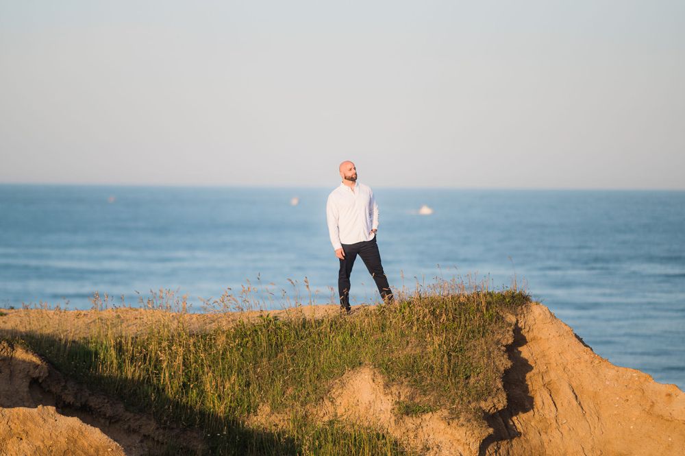 Groom standing at the edge of the cliff with his hands in his pockets, gazing into the distance. Engagement photos