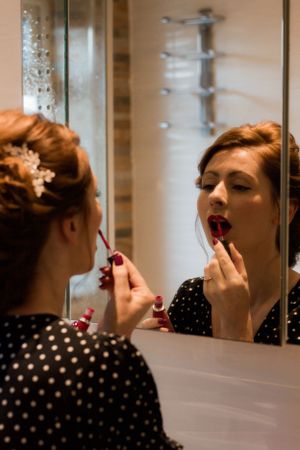 A polka dot dress being reflected in a bathroom mirror while applying lipstick.