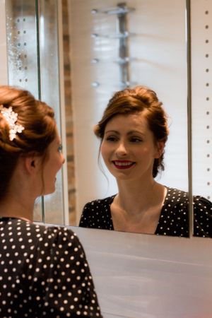 Classic vintage-inspired portrait in polka dot dress with red lipstick reflected in vanity mirrors.
