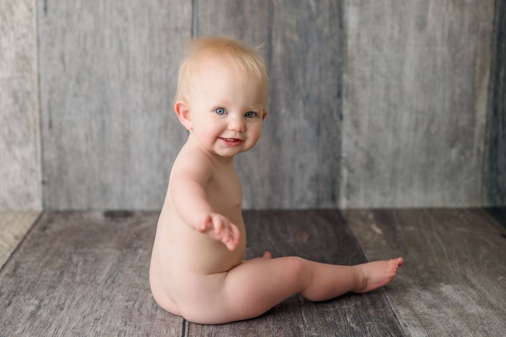 Happy baby sitting on rustic wooden floor during portrait session.