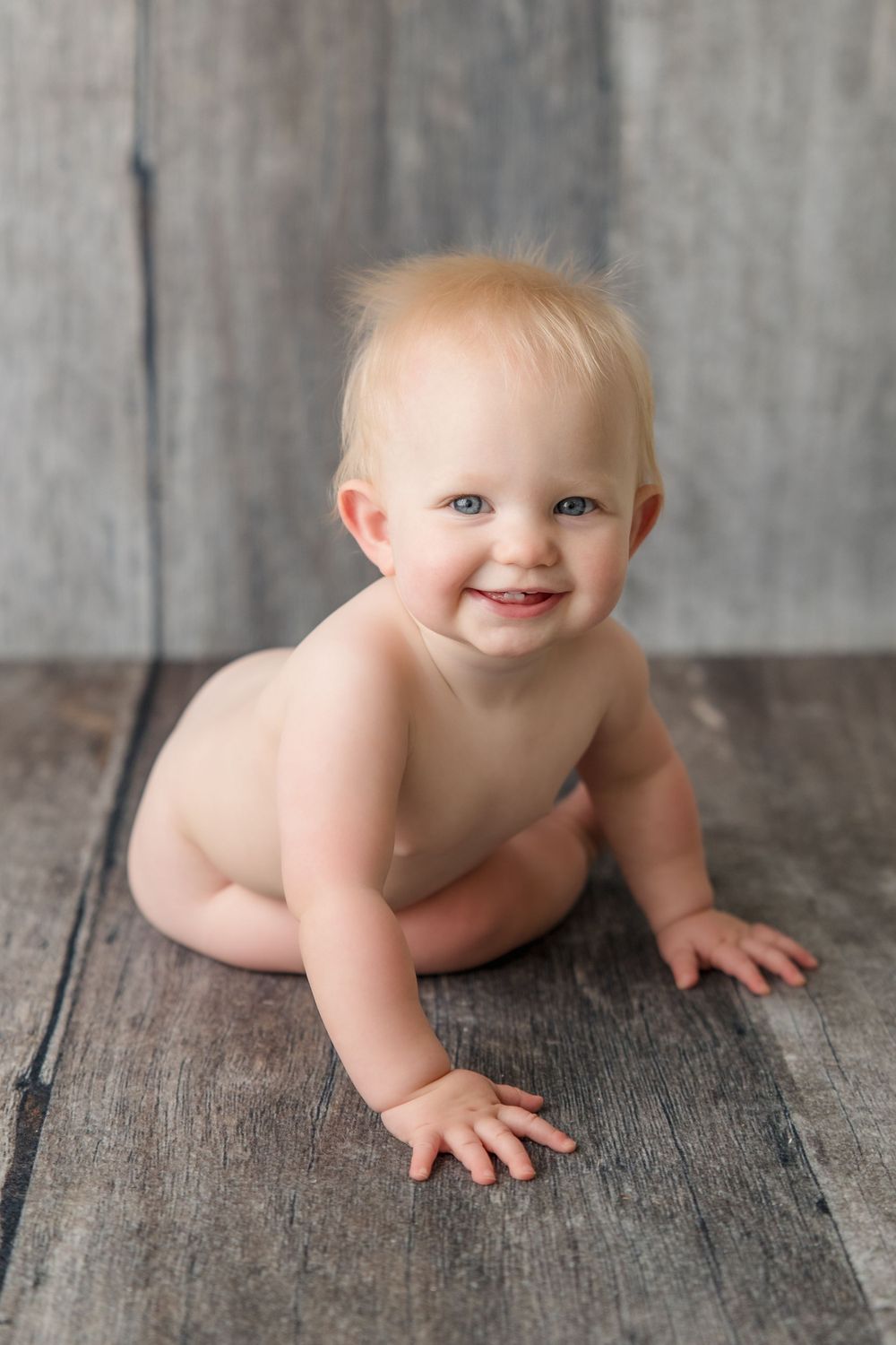 Smiling baby crawling on wooden floor during indoor photo shoot.