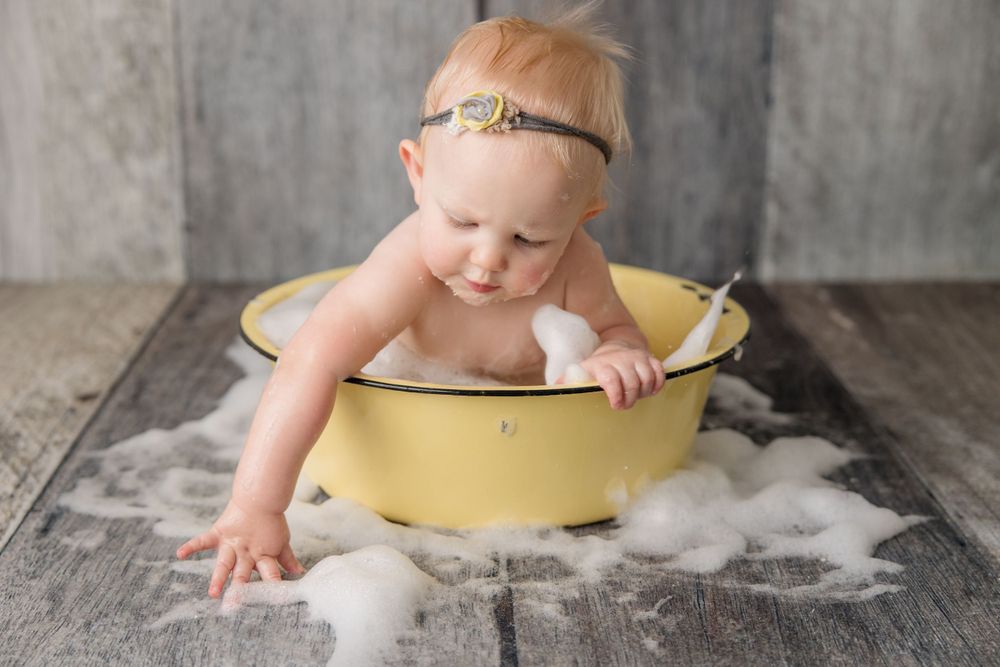 Baby playing in yellow vintage basin during rustic milk bath photography session.