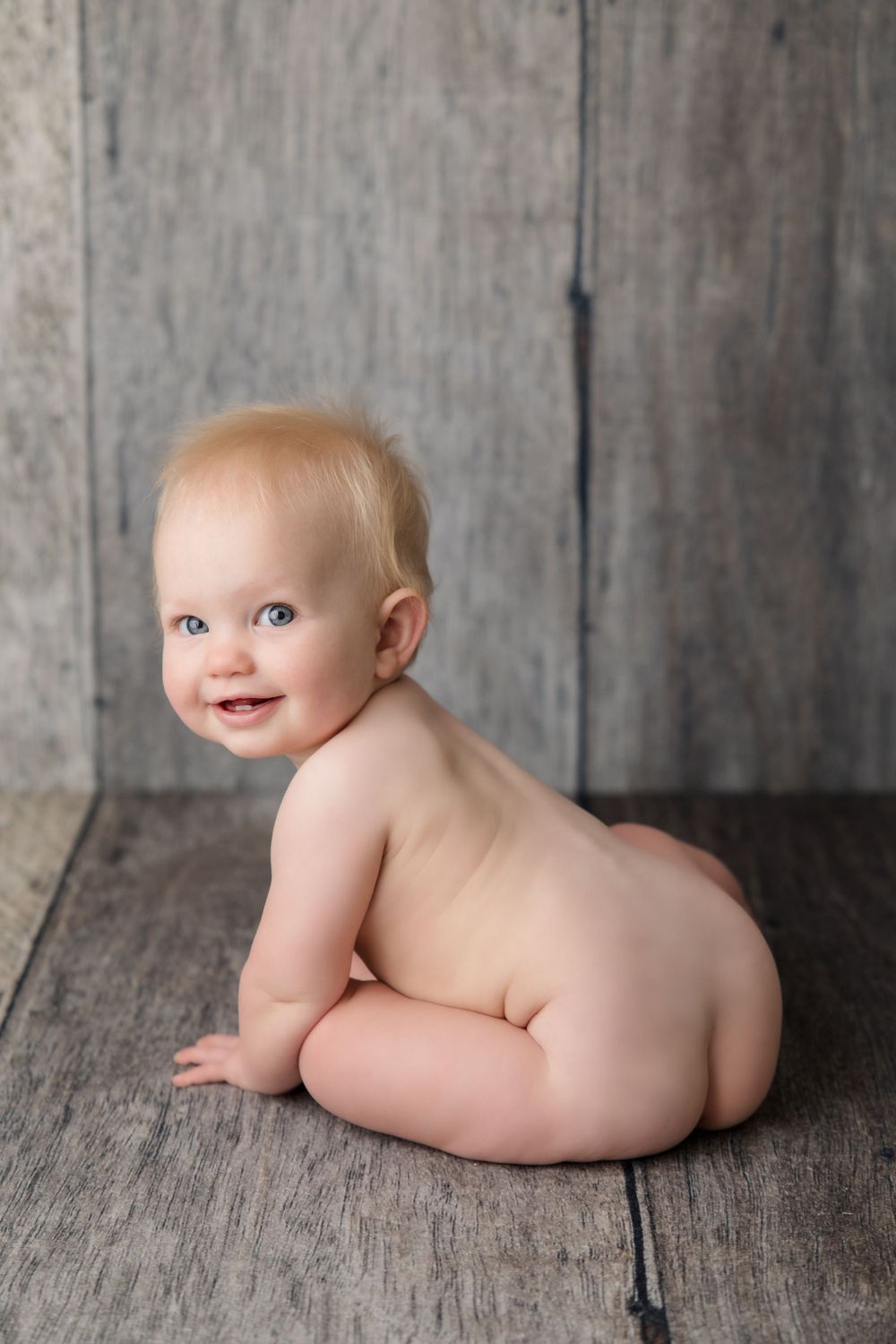 Baby crawling on wooden floor during artistic portrait session.