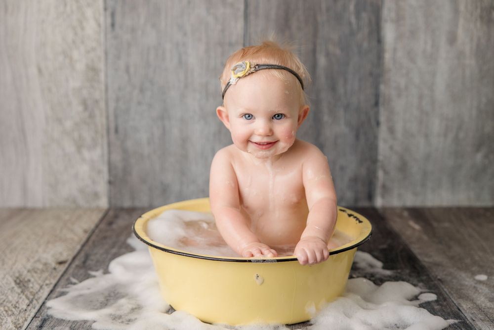 Baby sitting in large vintage yellow enamel basin for milestone photo session.