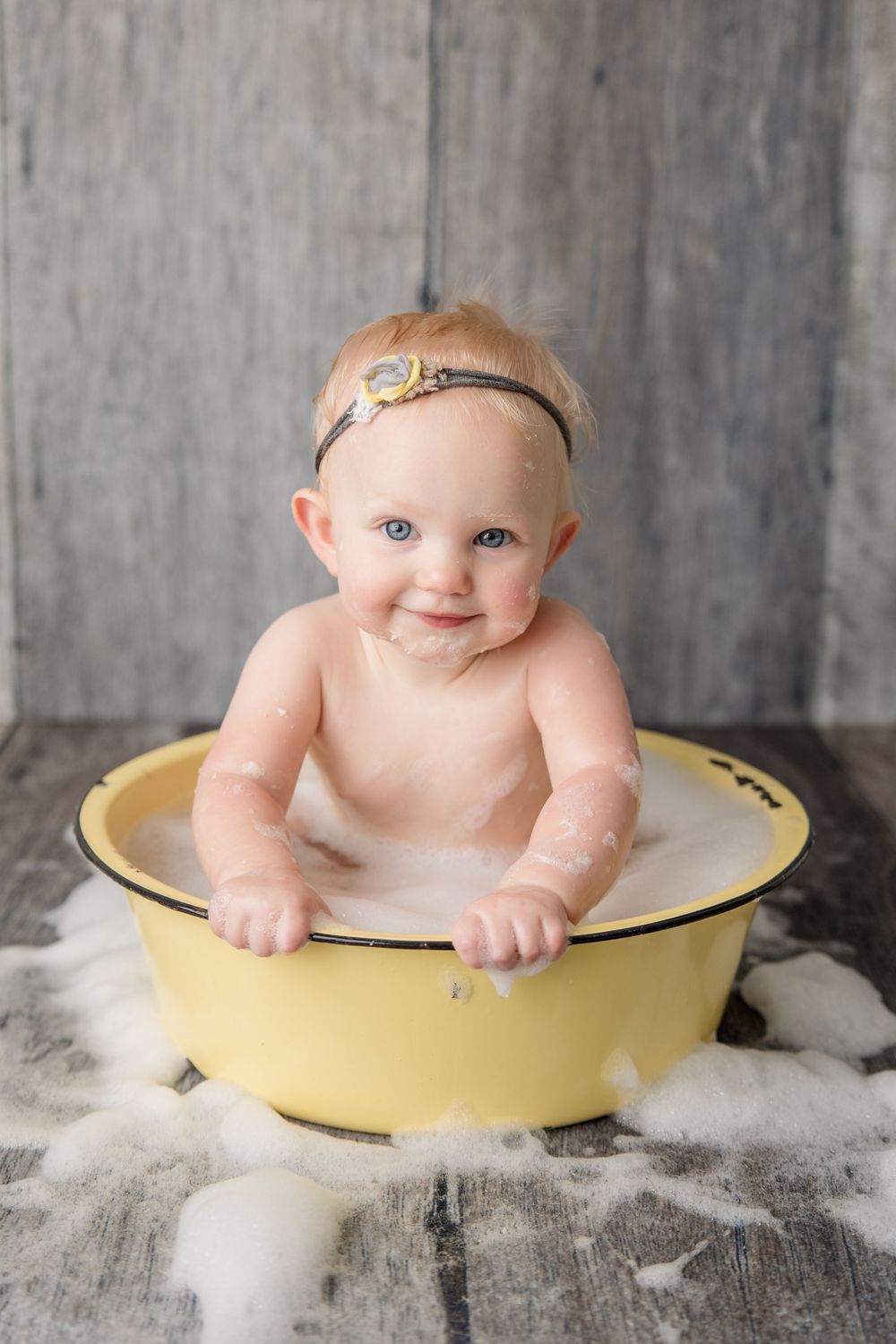 Baby in vintage milk bath photography setup with yellow enamel basin against gray backdrop.