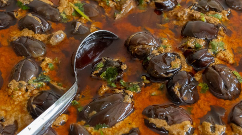 Simmering mushrooms in a rich orange-colored sauce with a serving spoon.