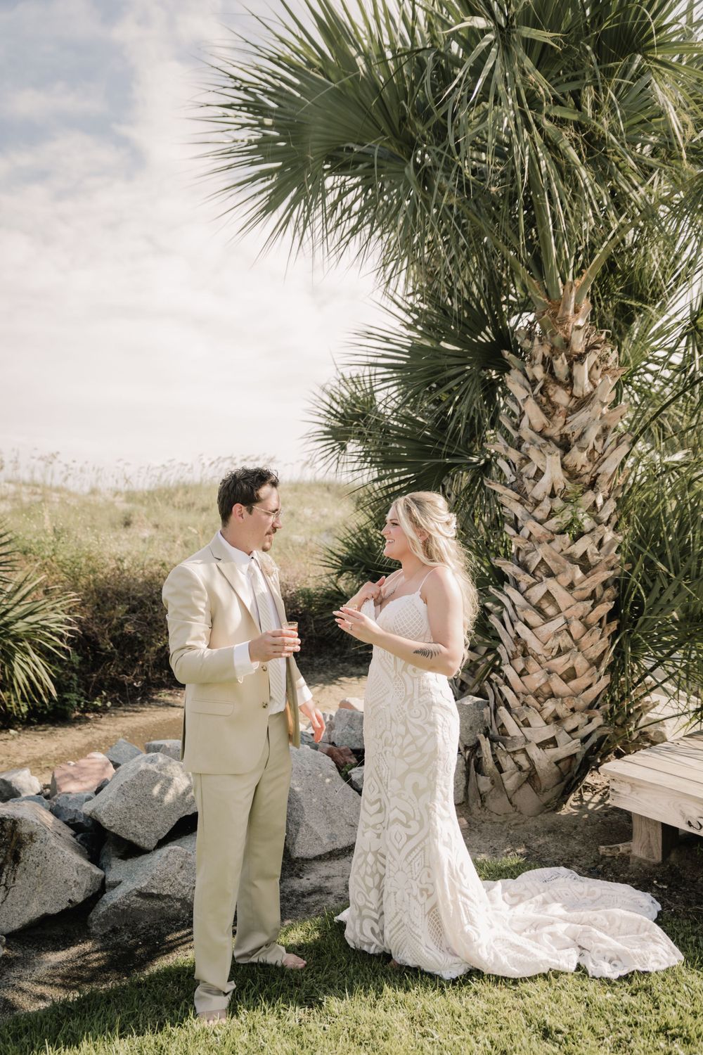 A bride in lace and groom in light suit having a conversation during their outdoor wedding.