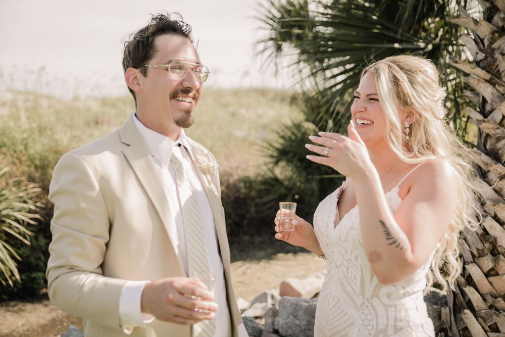 A couple shares a joyful moment during their outdoor wedding ceremony near palm trees.