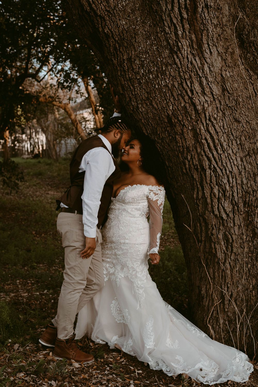 Romantic wedding couple poses against massive tree trunk in natural lighting.