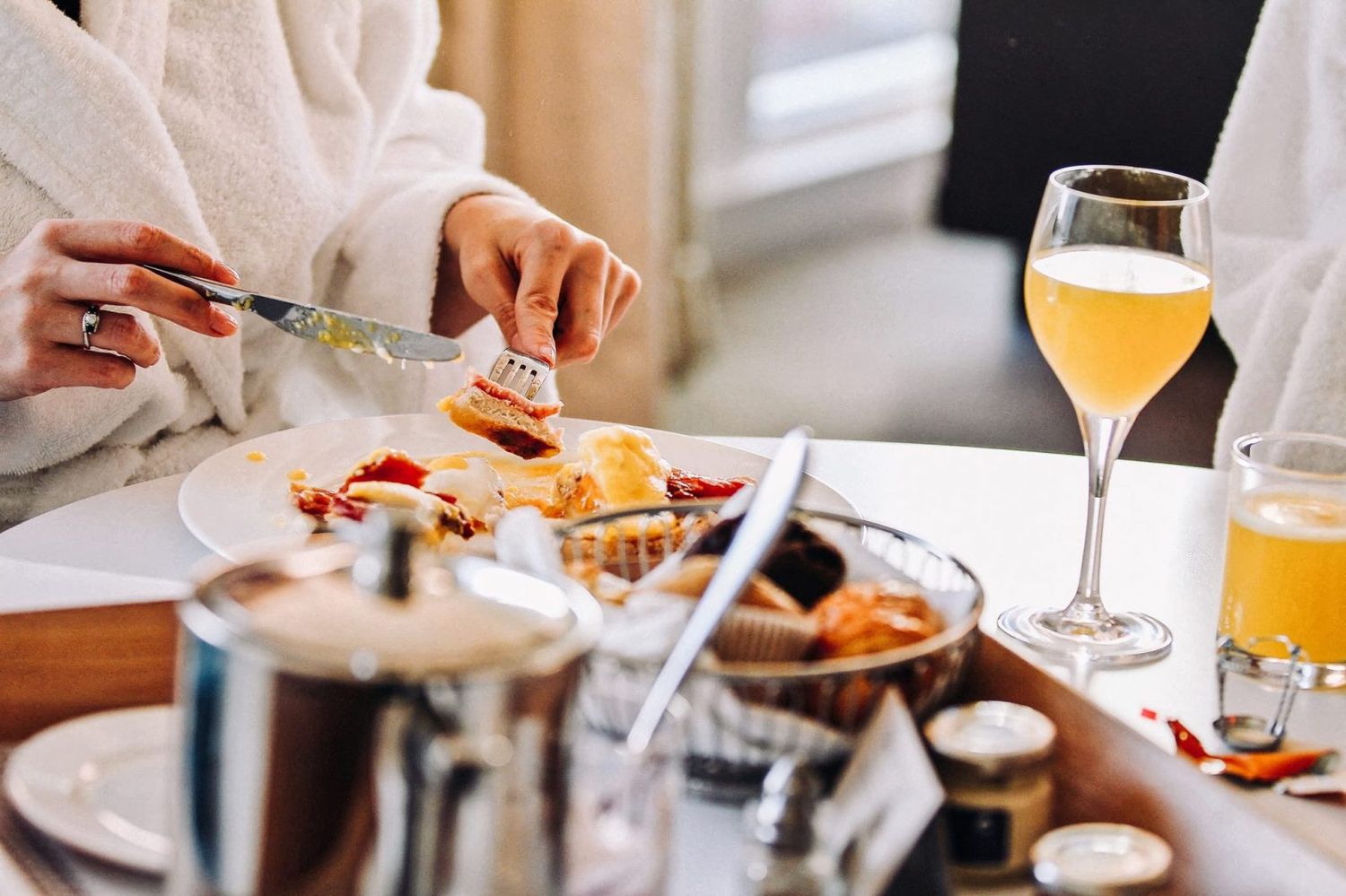 Close up of breakfast table with mimosas and person cutting food.