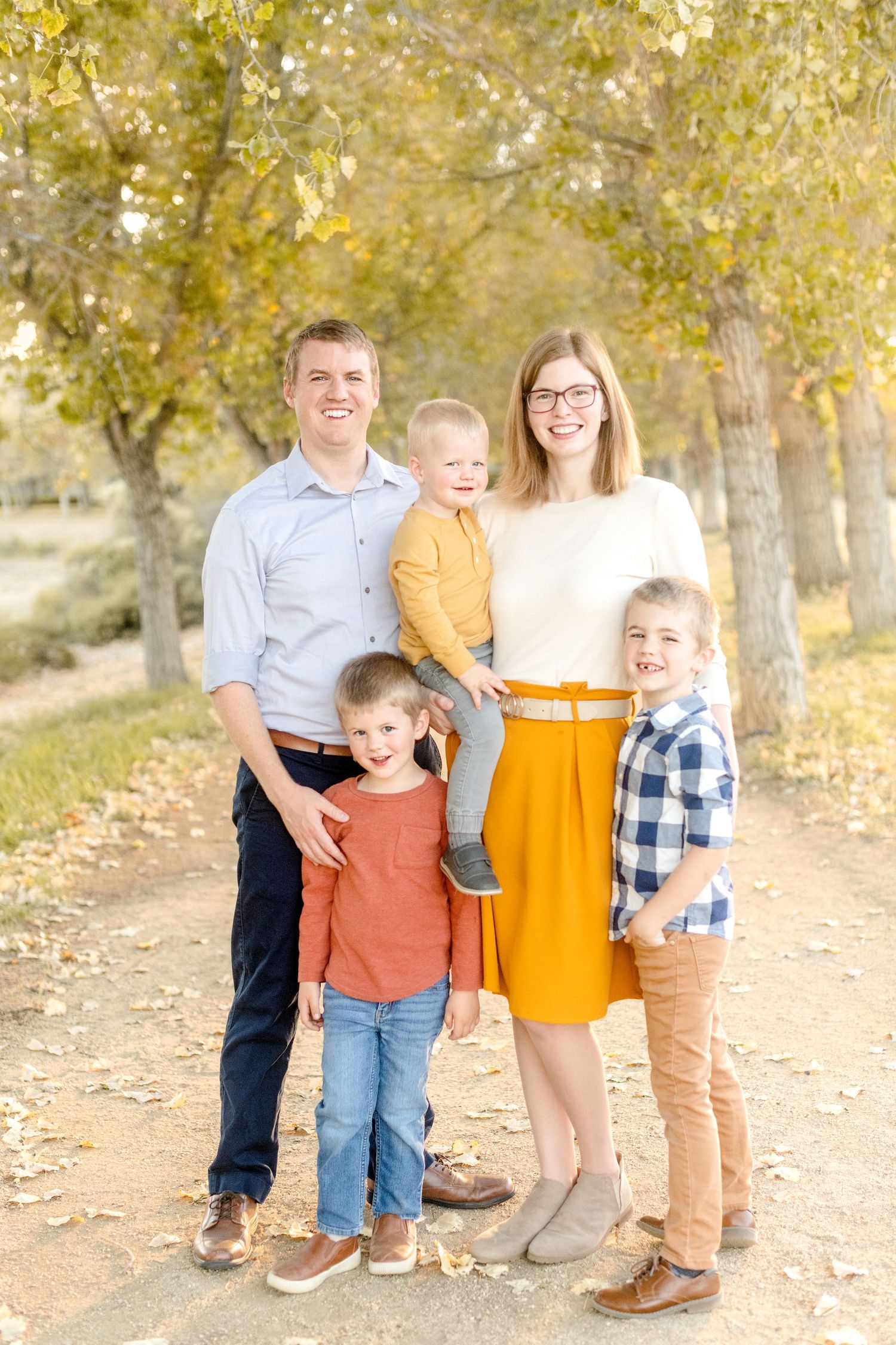 Family of five poses together on a path lined with yellow autumn trees.