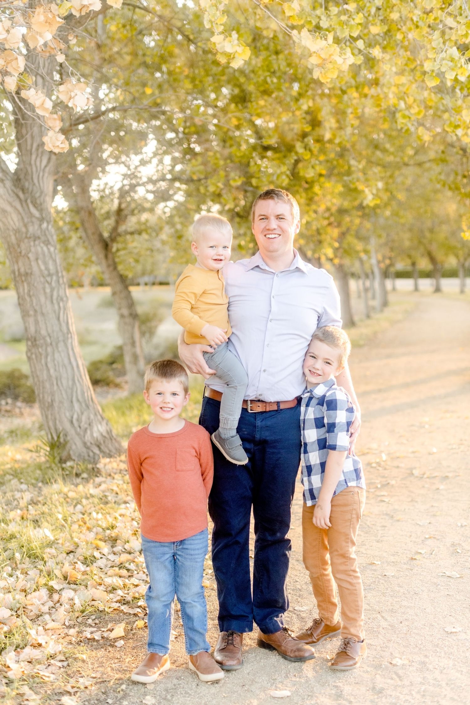 Four people pose together on tree-lined path during autumn season.