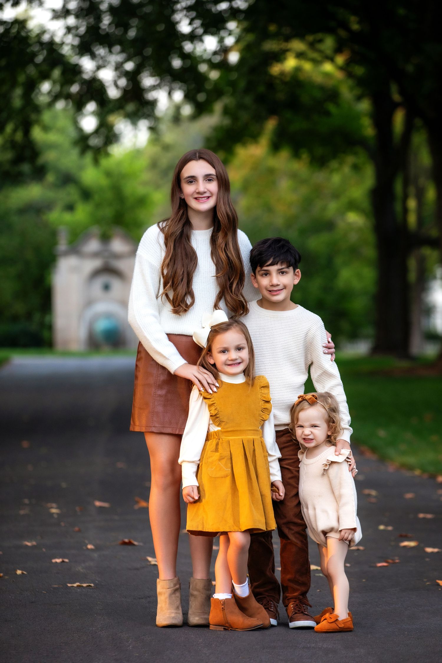 Family group wearing coordinated fall outfits poses on tree-lined path.