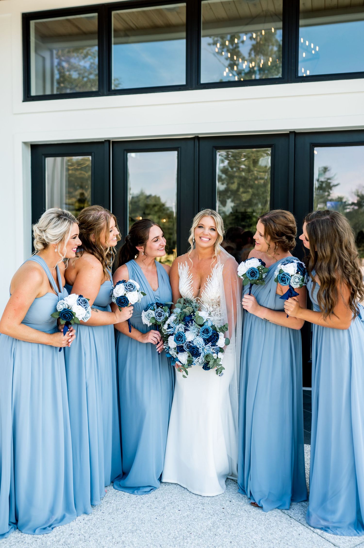 Bridesmaids in light blue dresses line up against white building for wedding photo.