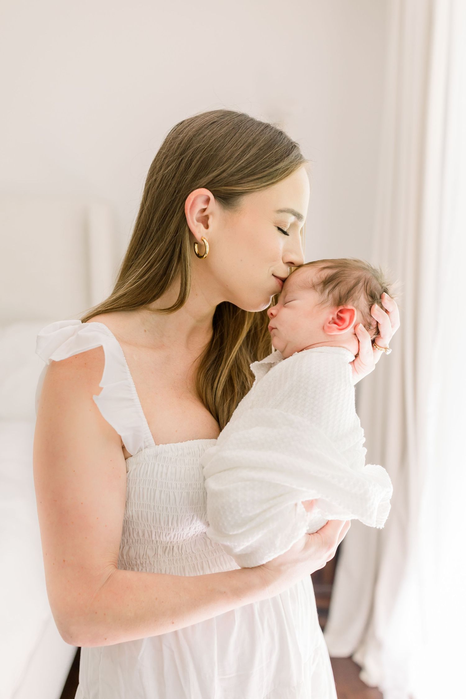 Gentle moment between parent and newborn baby swaddled in white.