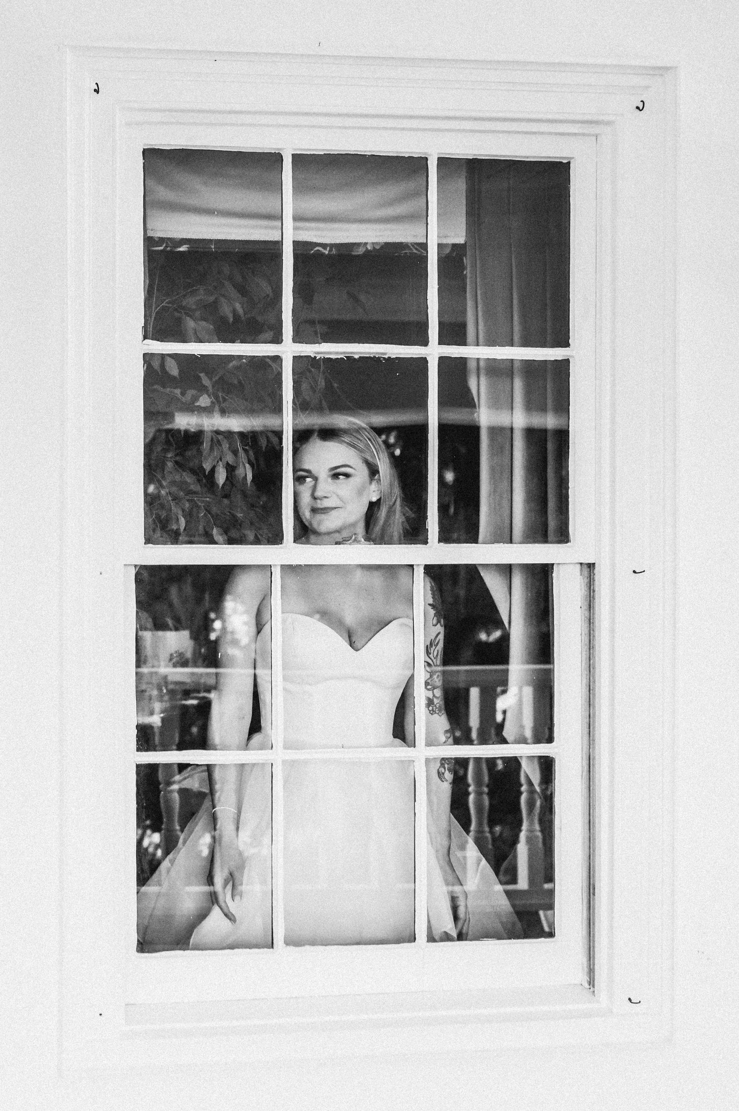 Artistic window frame composition of a bride in white against a bright interior.