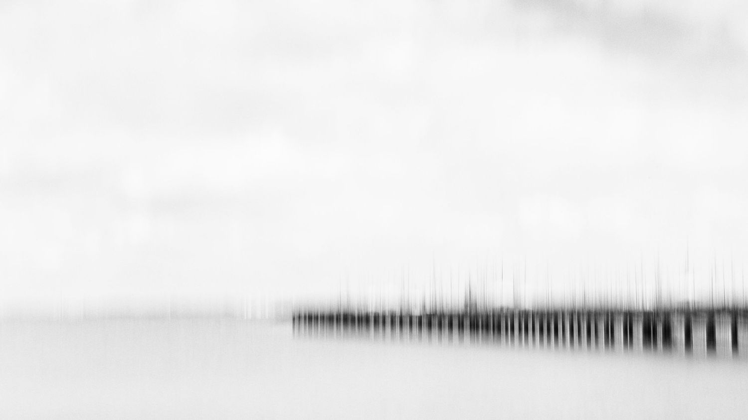 Minimalist black and white pier extends into misty horizon creating ethereal seascape composition.