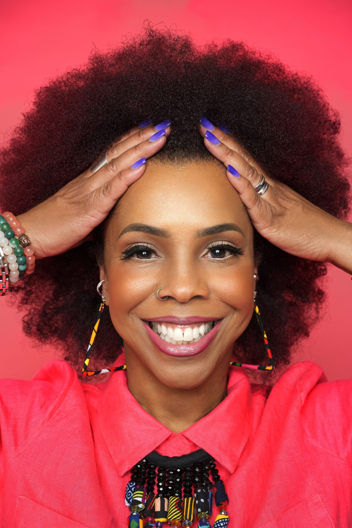 Vibrant portrait against red background with colorful jewelry and bright makeup.