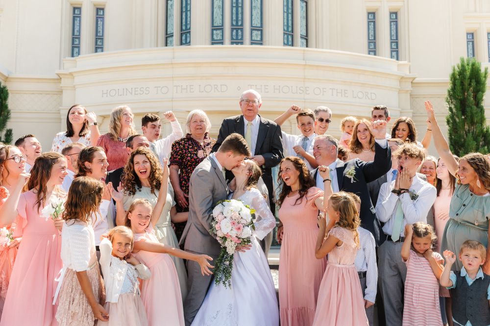 Joyful wedding celebration with large group gathered at ornate white temple entrance.