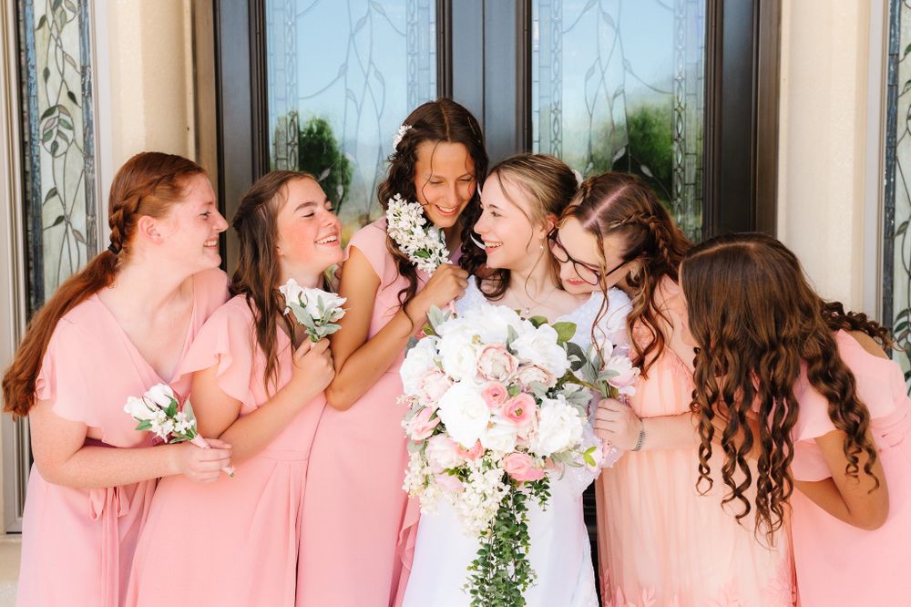 Bridesmaids in pink dresses share candid laughing moment during wedding photos.