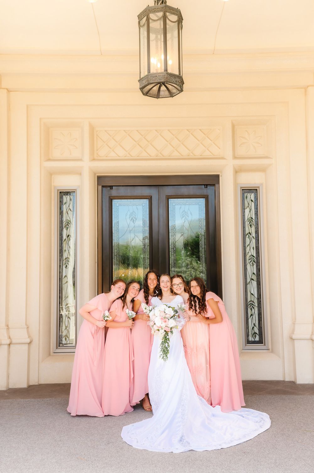 Wedding party in pink dresses and white gown gathered on a light colored porch.