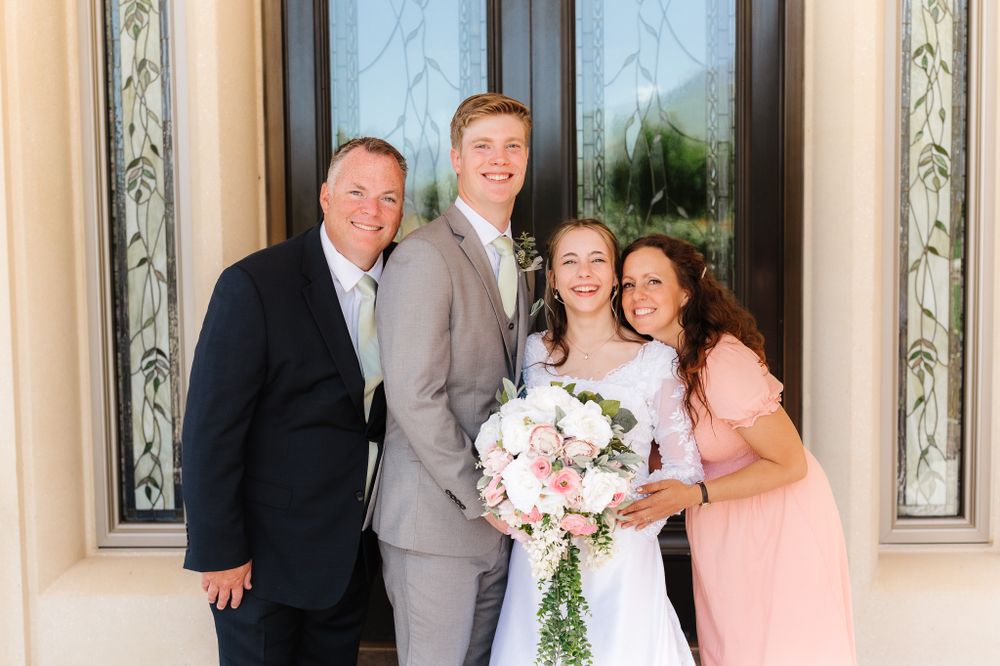 Wedding party posing together in formal attire outside a building.