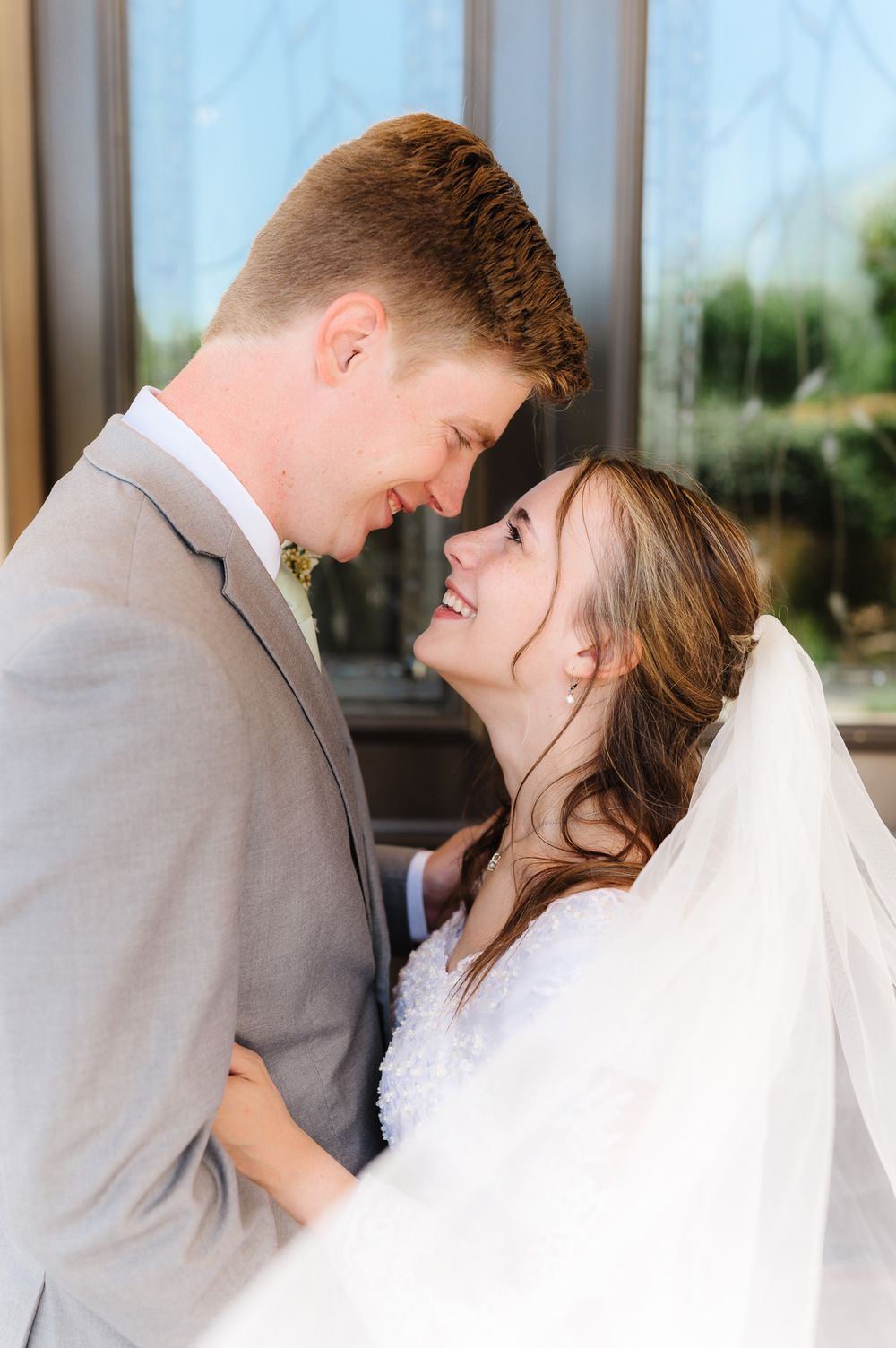 Wedding couple sharing an intimate moment under natural light indoors.