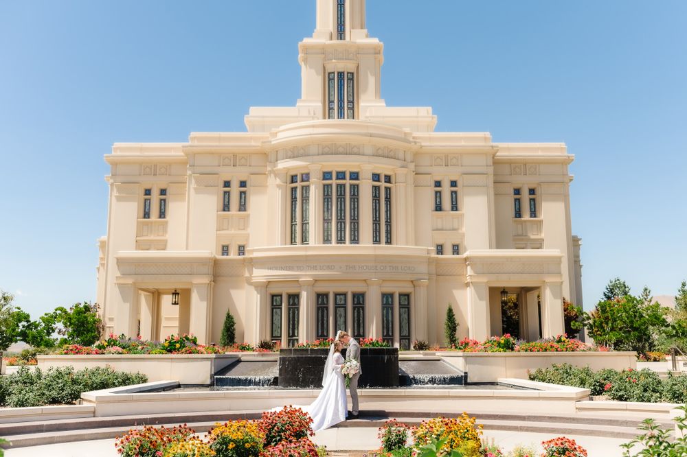 A wedding couple stands centered before a symmetrical white temple with manicured gardens.