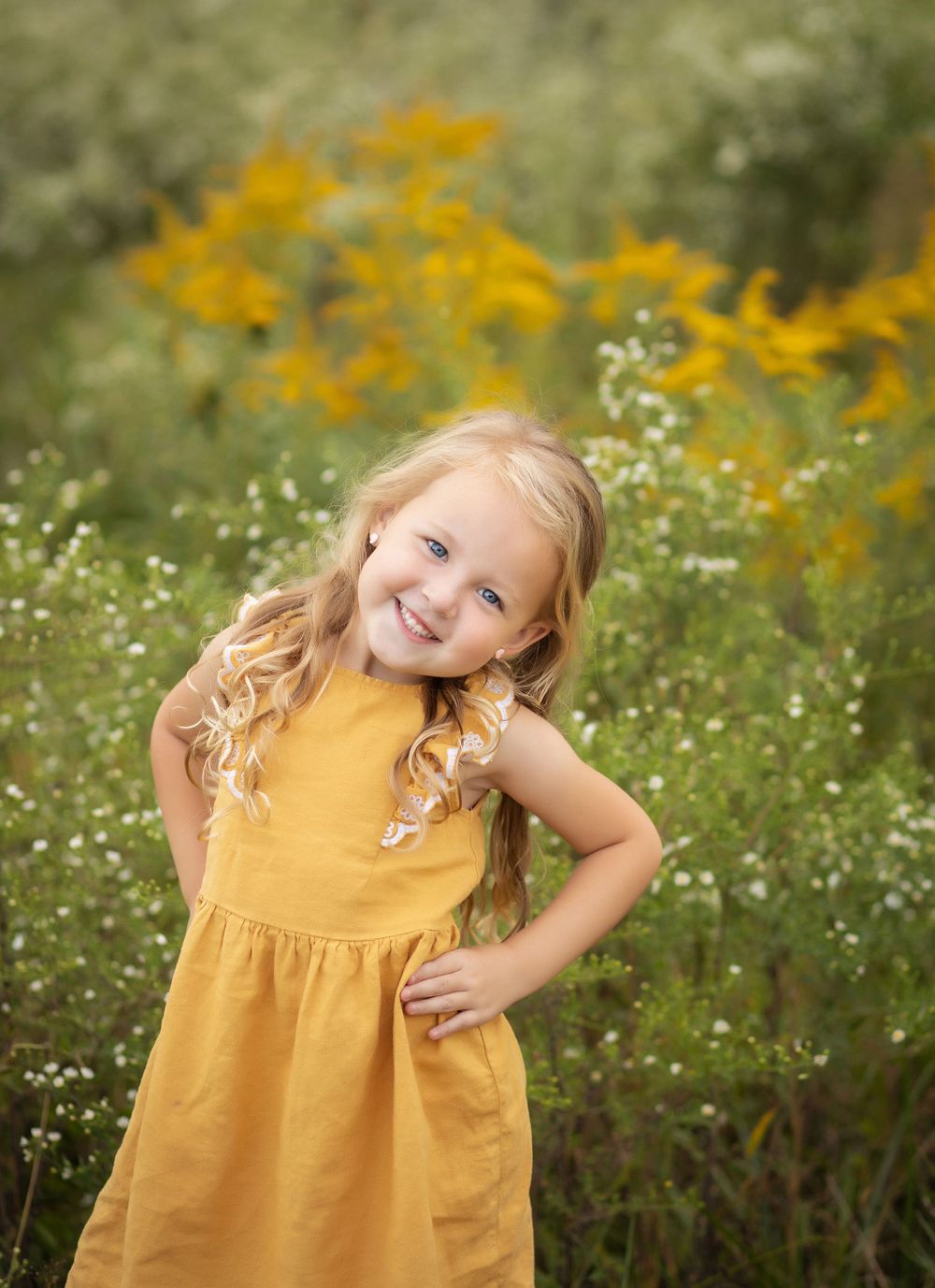 Portrait in wildflower field with yellow dress matching golden blooms.
