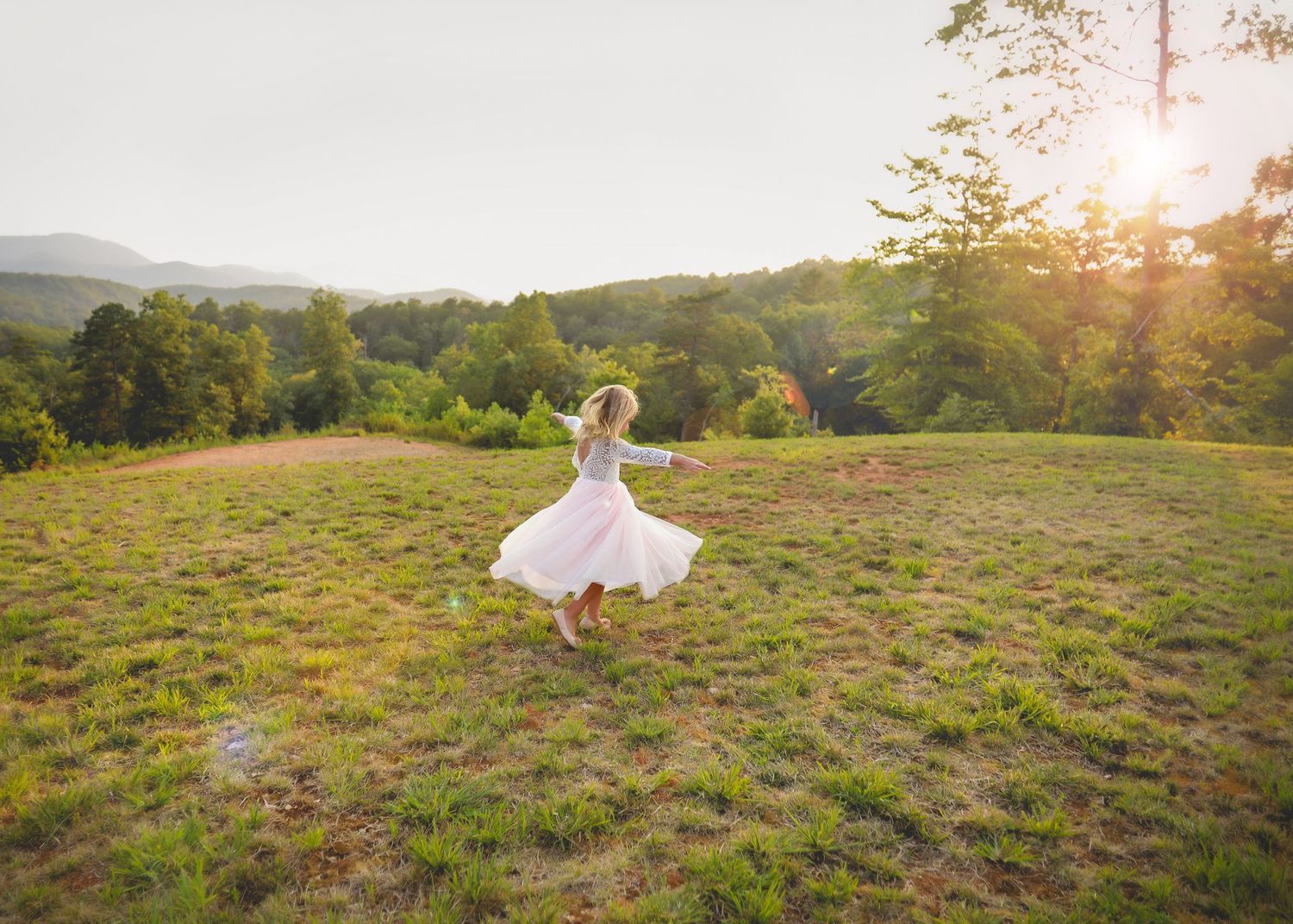 Person in white dress running through grassy field at sunset.