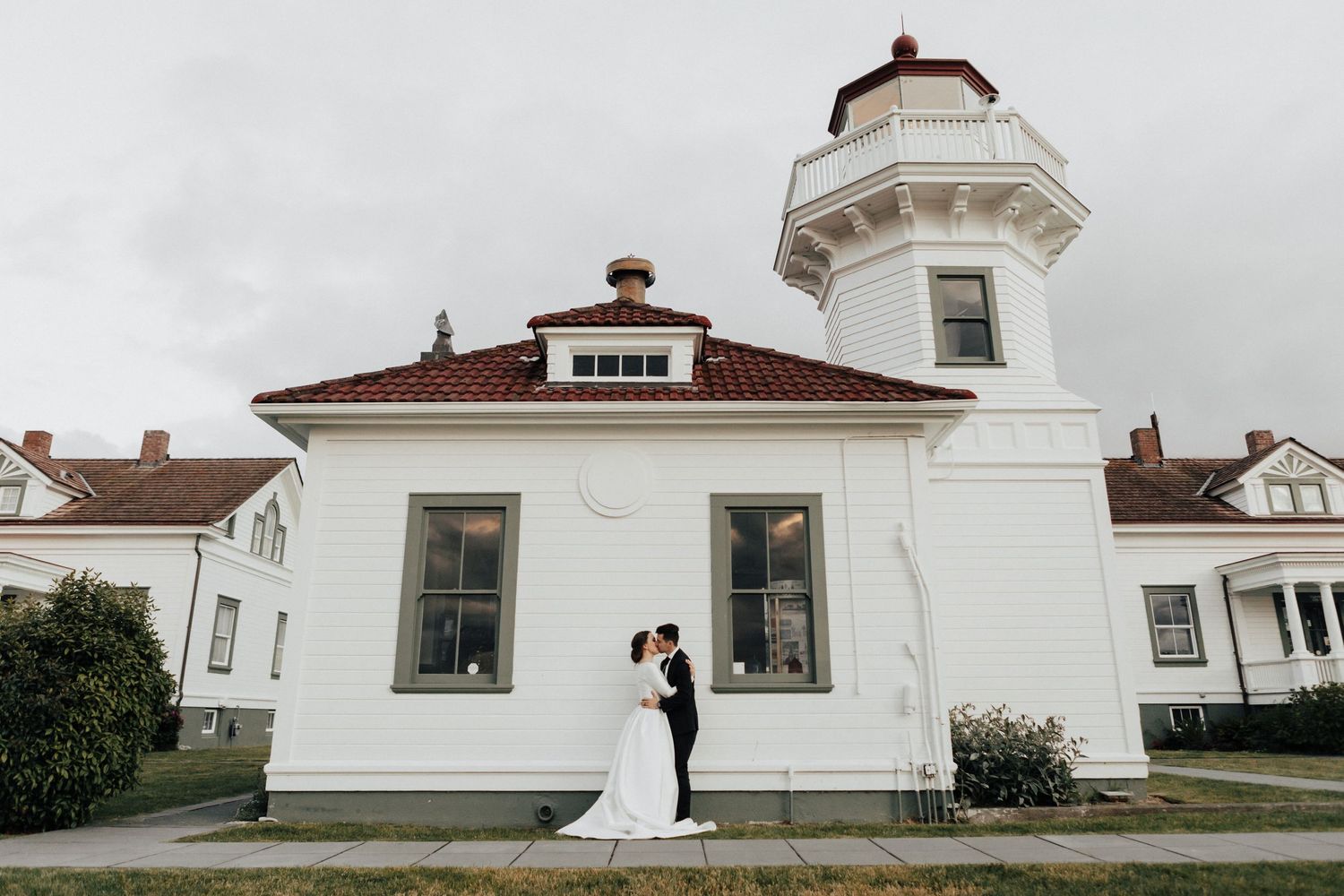 A classic wedding portrait in front of a white lighthouse with red roof.