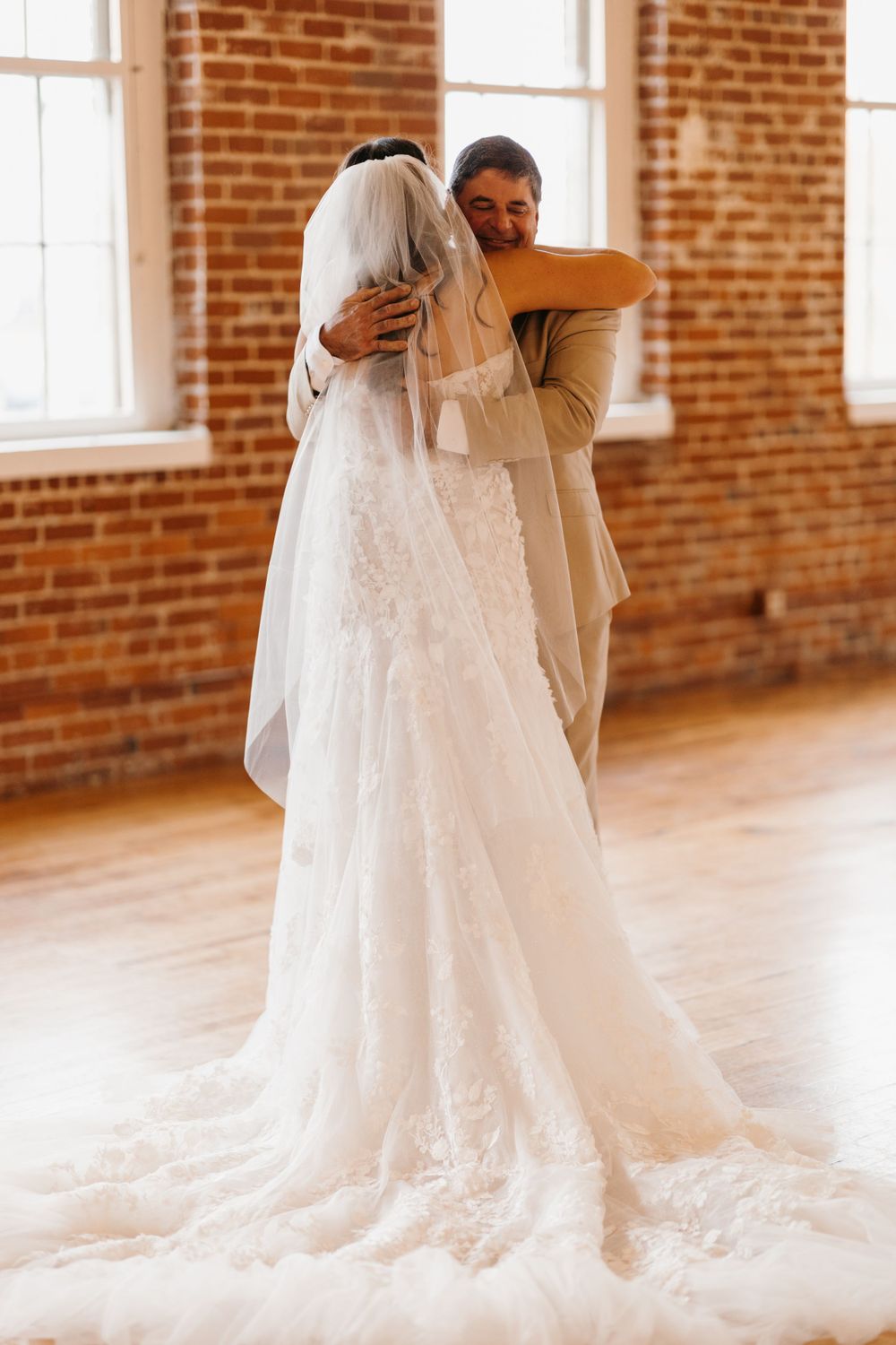 Bride and groom share emotional embrace during first look in rustic brick-walled wedding venue.