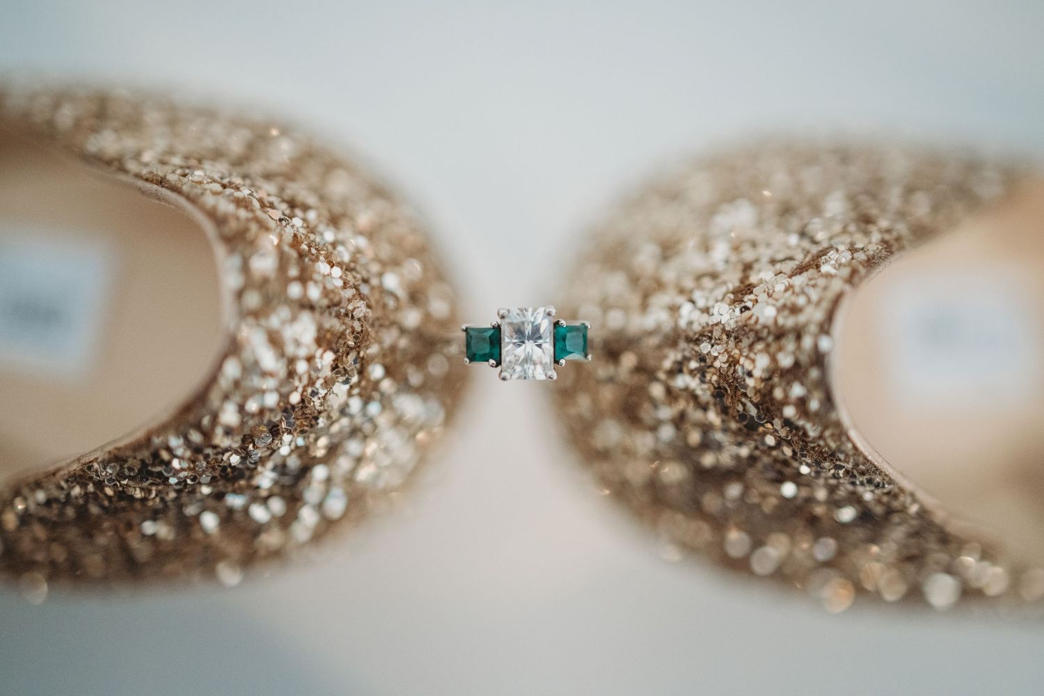 Wedding ring with emerald stone between sparkly gold glitter shoes.