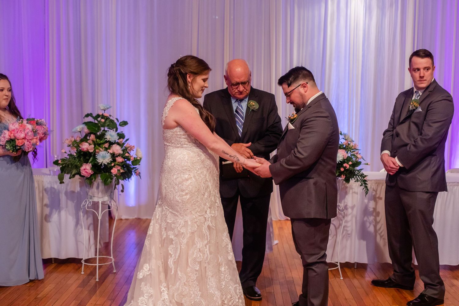 Wedding celebration in a beautifully lit reception hall with purple uplighting and white drapes.